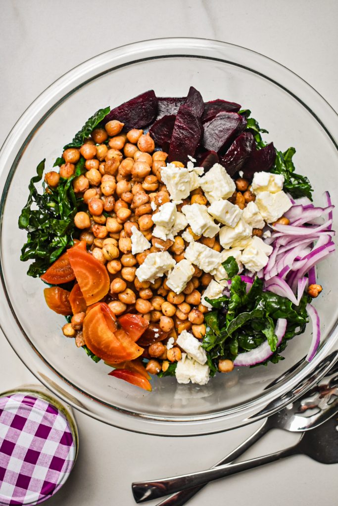 Top view of the kale, roasted chickpeas, roasted beets, onion, feta cheese in a mixing bowl.