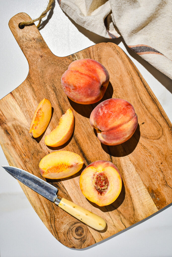 Peaches being sliced on a wooden cutting board.