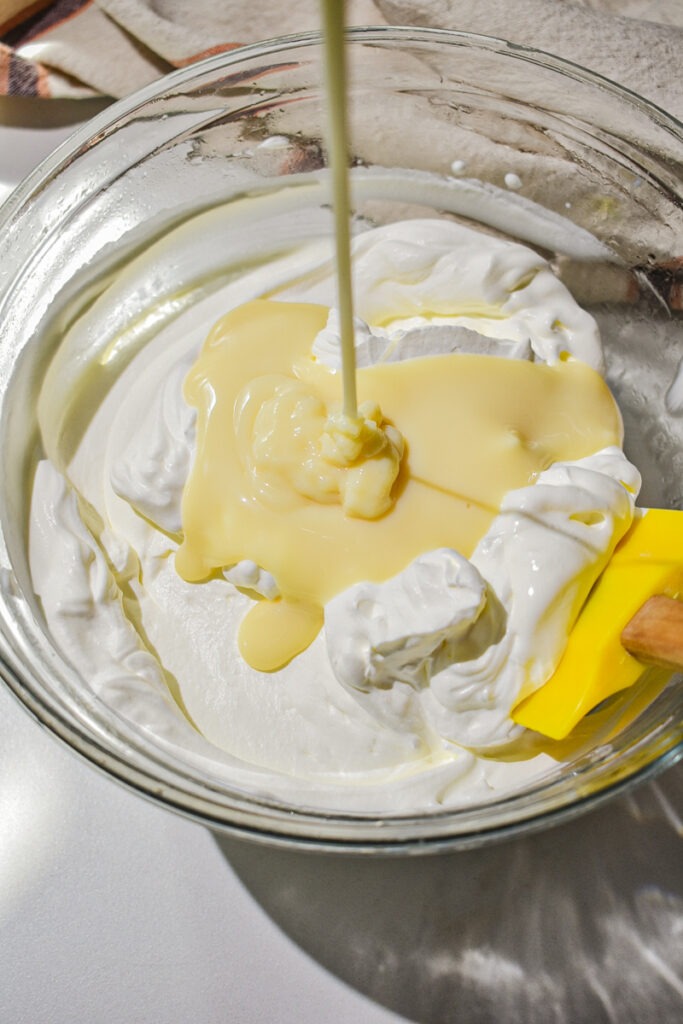 Pouring condensed milk into the whipped cream.