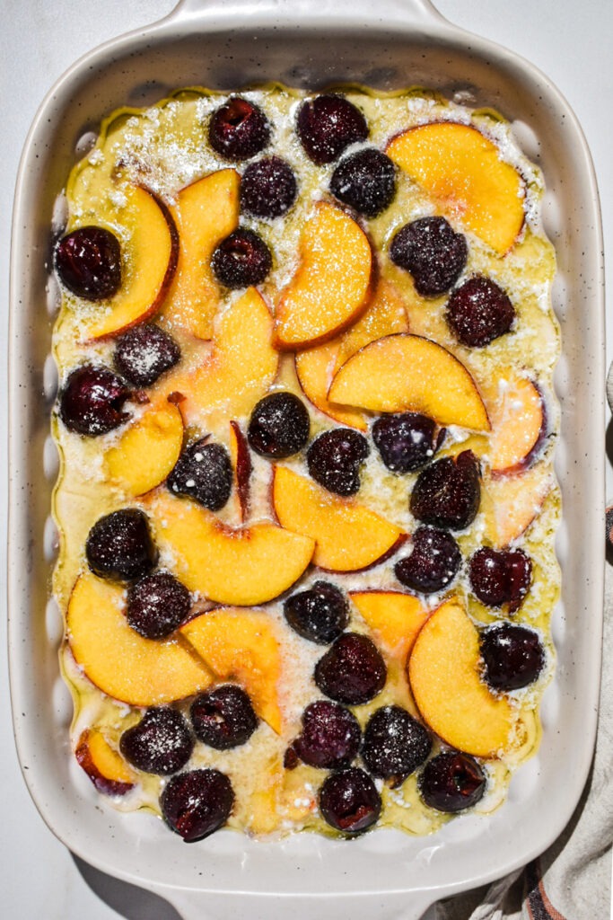 Peaches and cherries added to the melted butter in a baking dish.