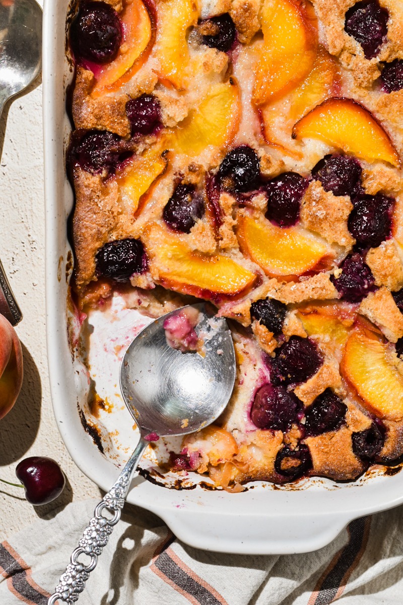 Overhead shot of peach cobbler in a white baking dish with a portion missing and a spoon.