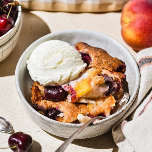 Serving of peach cobbler in a bowl with vanilla ice cream on top.