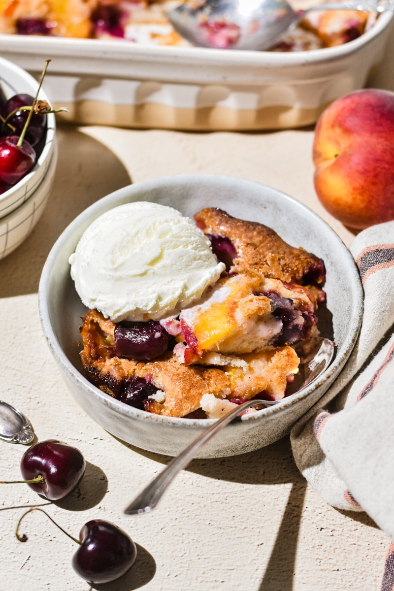 Serving of peach cobbler in a bowl with vanilla ice cream on top.