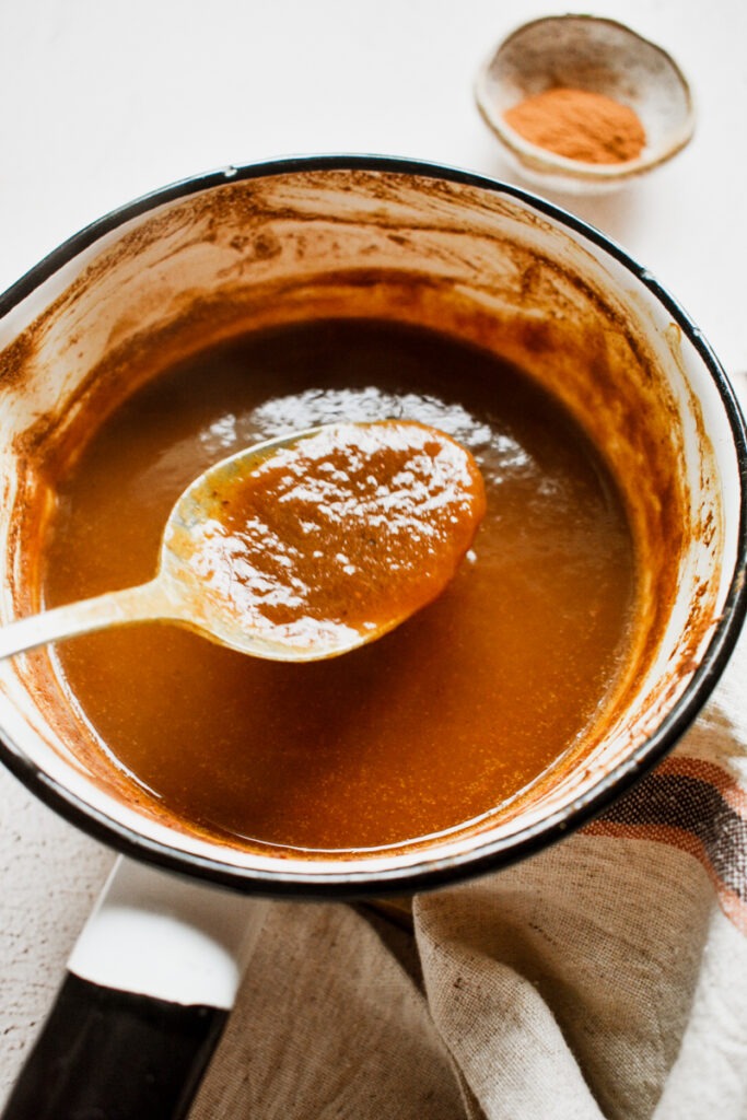 Spoon holding up some of the pumpkin sauce from the saucepan.