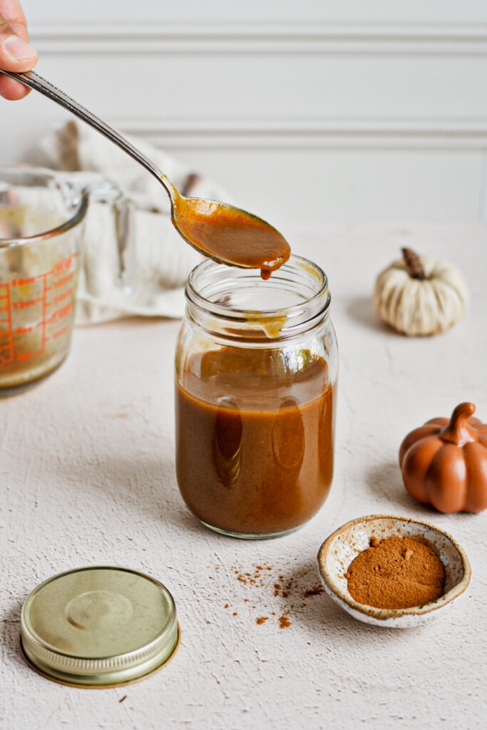 Hand holding a spoonful of homemade pumpkin sauce above the jar.