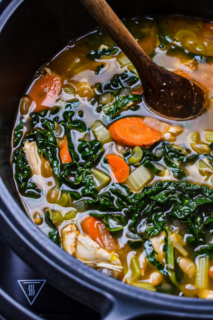 Kale added to the chicken soup in a pot.