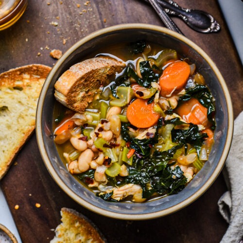 Overhead shot of chicken white bean kale soup in a bowl next to crusty bread.