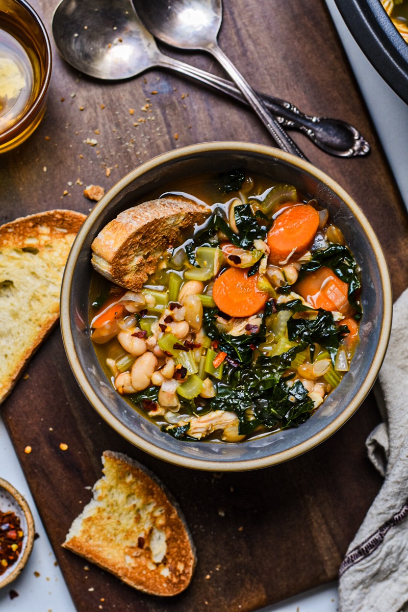 Overhead shot of chicken white bean kale soup in a bowl next to crusty bread.