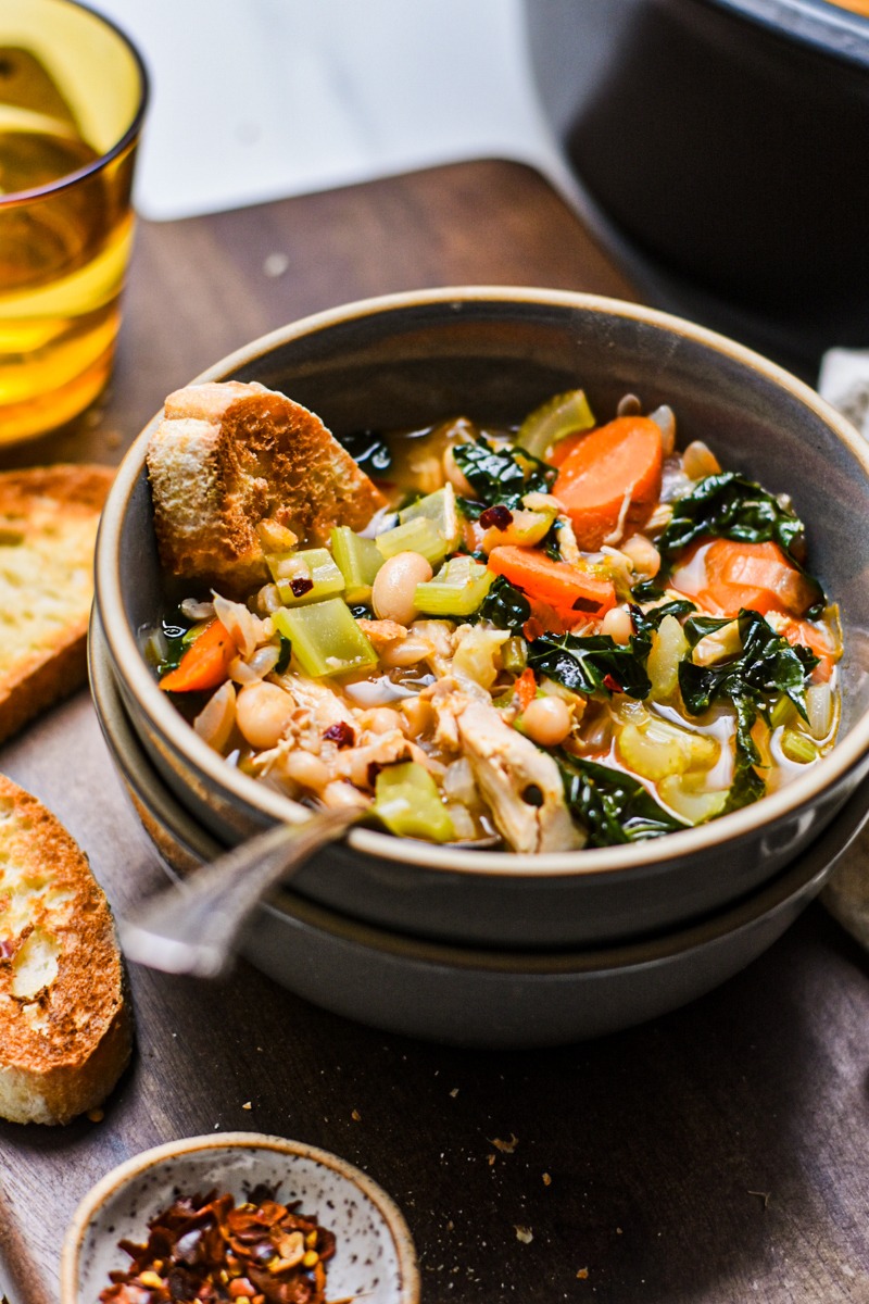 Bowl of chicken white bean and kale soup with bread and a spoon.