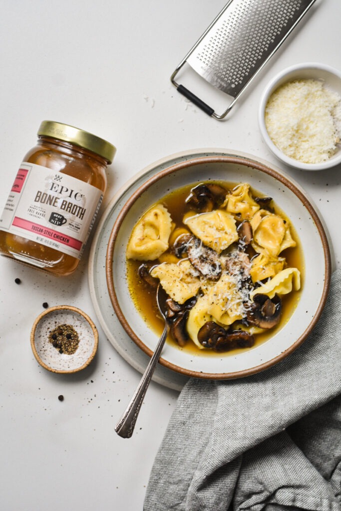 Bowl of tortellini in brodo next to a jar of bone broth.