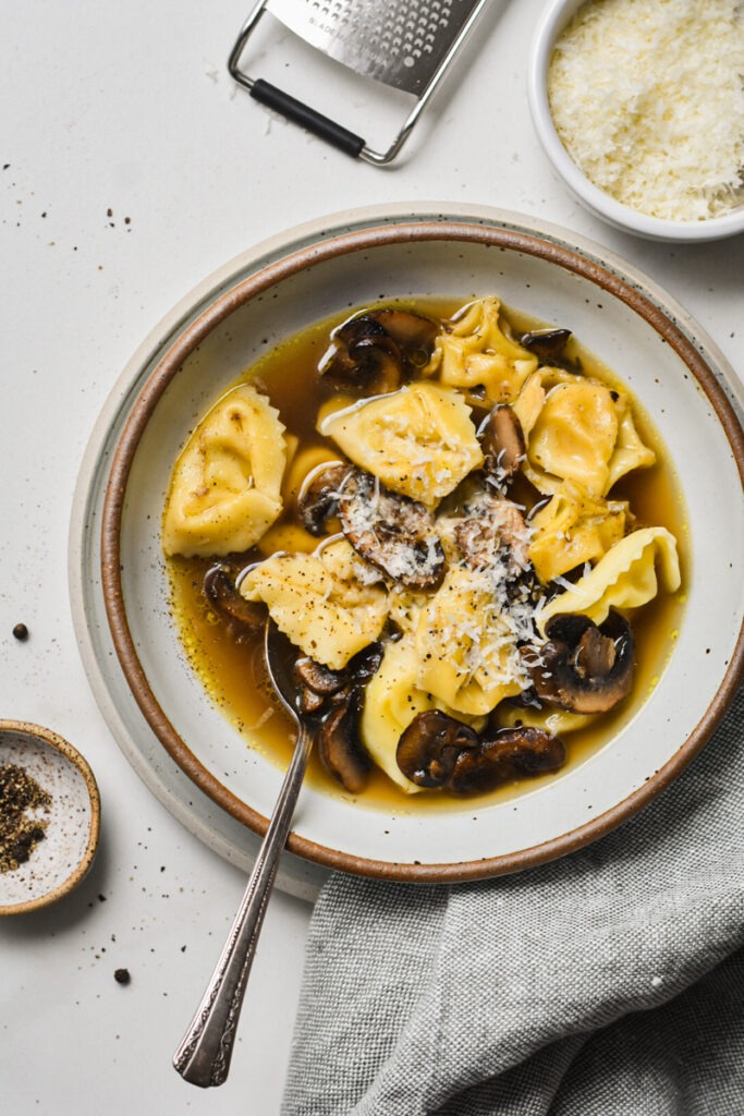 Overhead shot of tortellini in brodo with mushrooms topped with parm.