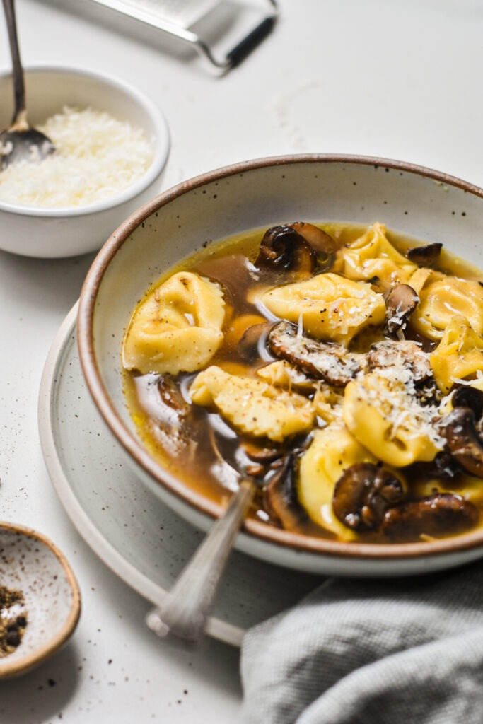 Side view of tortellini in brodo with mushrooms in a bowl garnished with parmesan.
