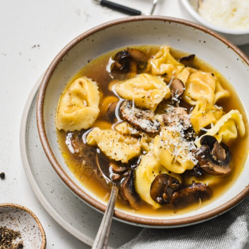 Tortellini in brodo with mushrooms served in a speckled bowl.