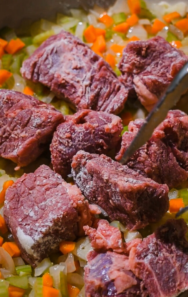 Adding the beef chunks to the pot to brown.
