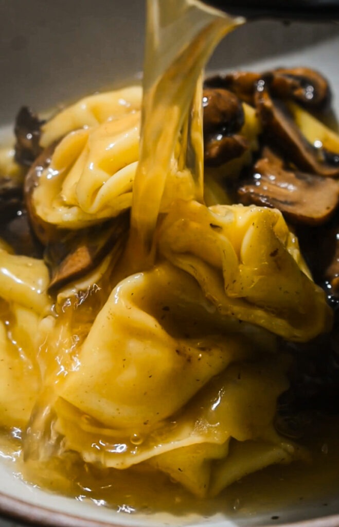 Pouring the broth over the tortellini and mushrooms in a bowl.