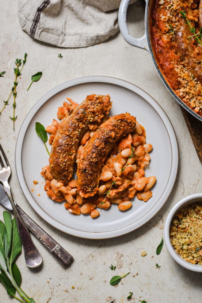 Portion of white bean and sausage cassoulet with two sausages on a plate.