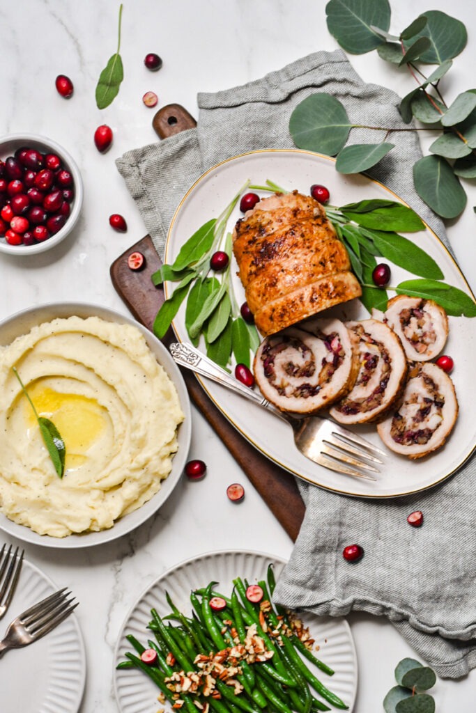 Turkey roulade on a plate with slices off the end served with mashed potatoes.