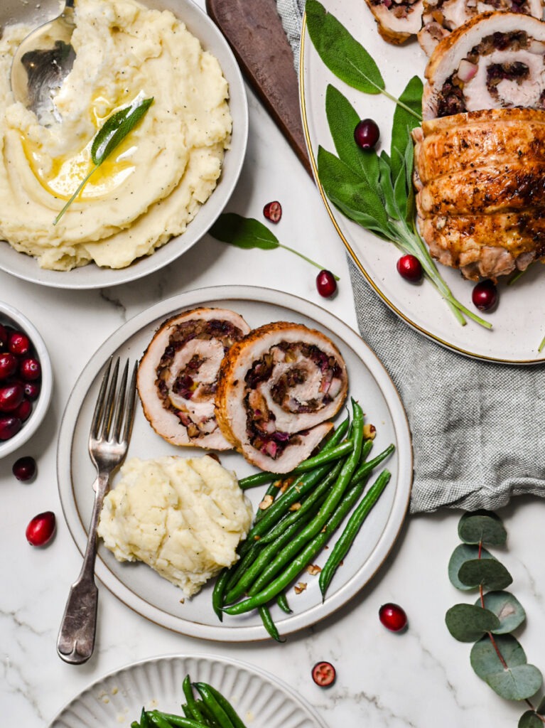 Turkey roulade served on a plate with mashed potatoes and green beans.
