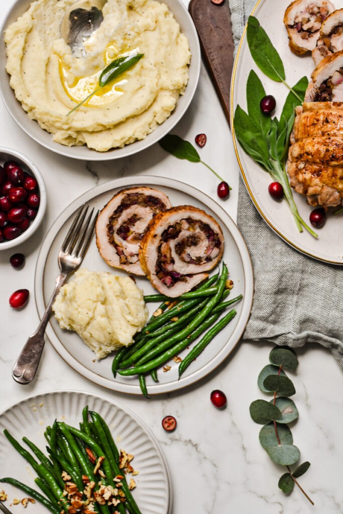 Two slices of turkey roulade on a plate with mashed potatoes and green beans.