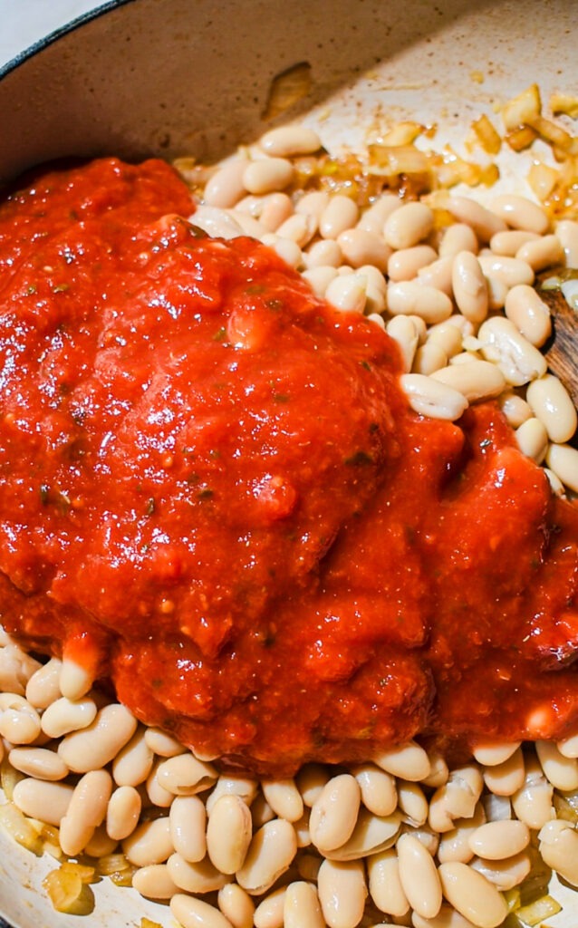 Adding the beans and tomato sauce to the skillet with onions.