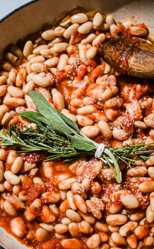 Adding the bouquet garni of herbs to the beans and tomatoes.