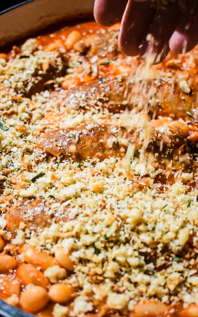 Topping the bean and sausage mixture with breadcrumbs to bake.