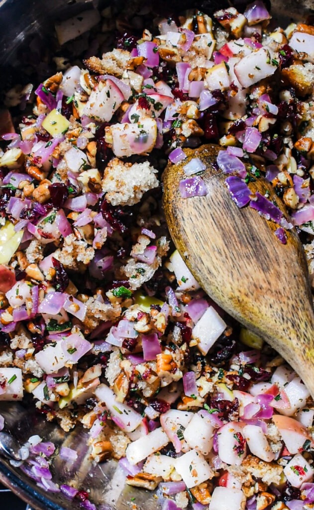 Sautéing the apple pecan cranberry filling in a skillet with a wooden spoon.