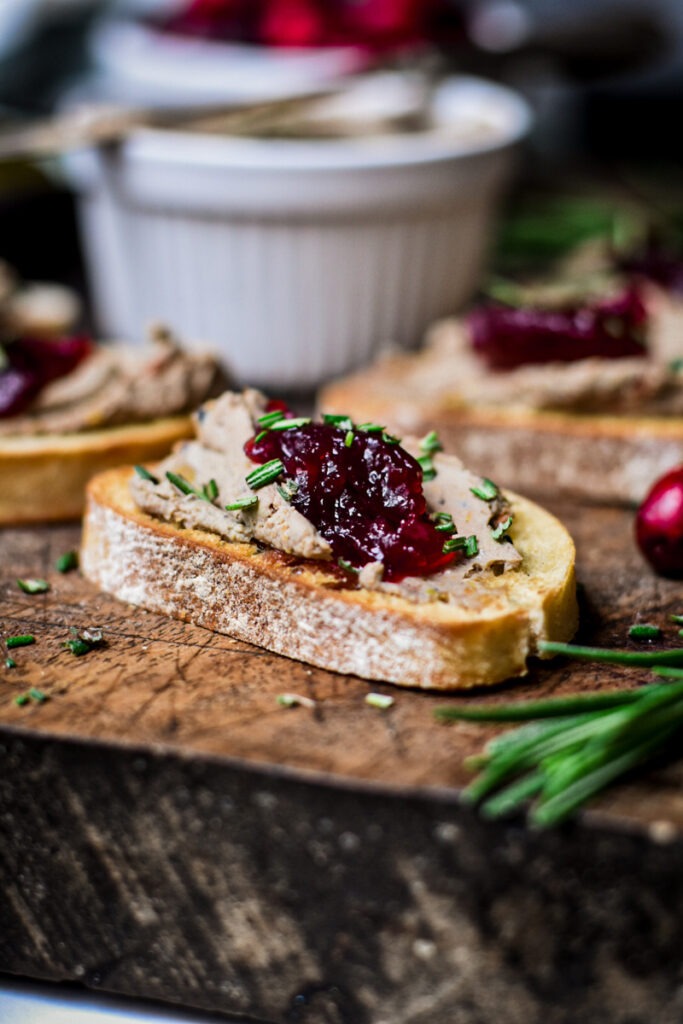 Side view of chicken liver pate served on a crostini with jam and chopped rosemary on top.