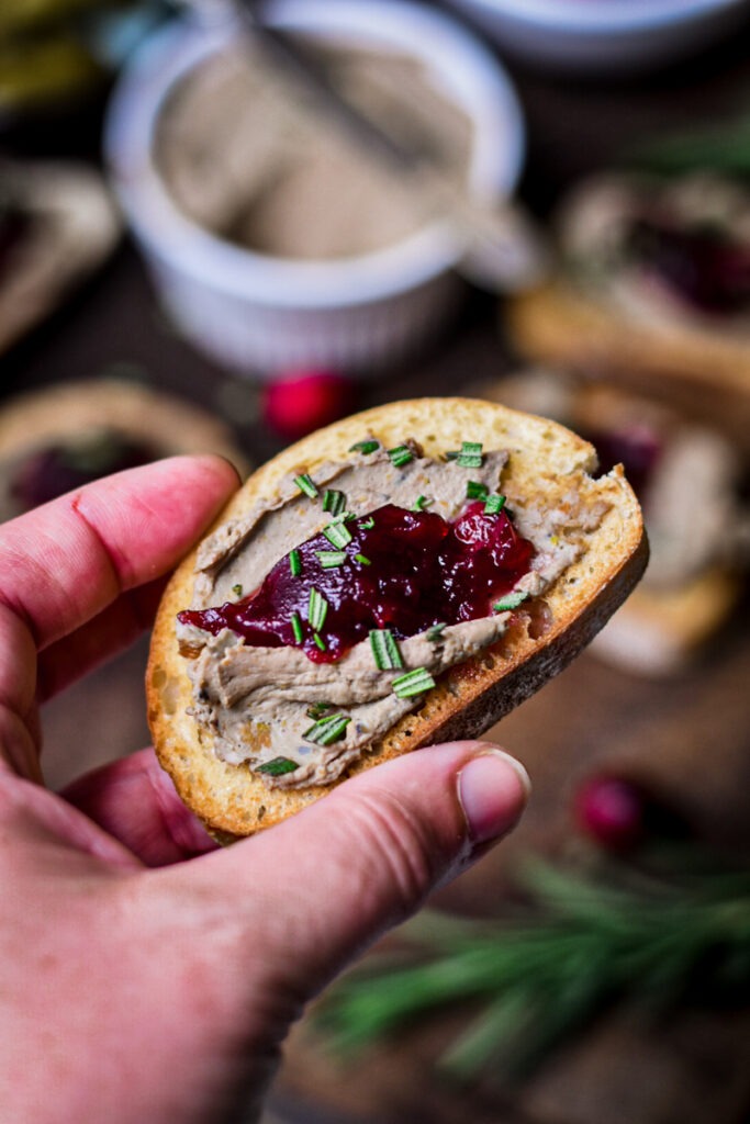 Hand holding a piece of bread with chicken liver pate and jam on top.