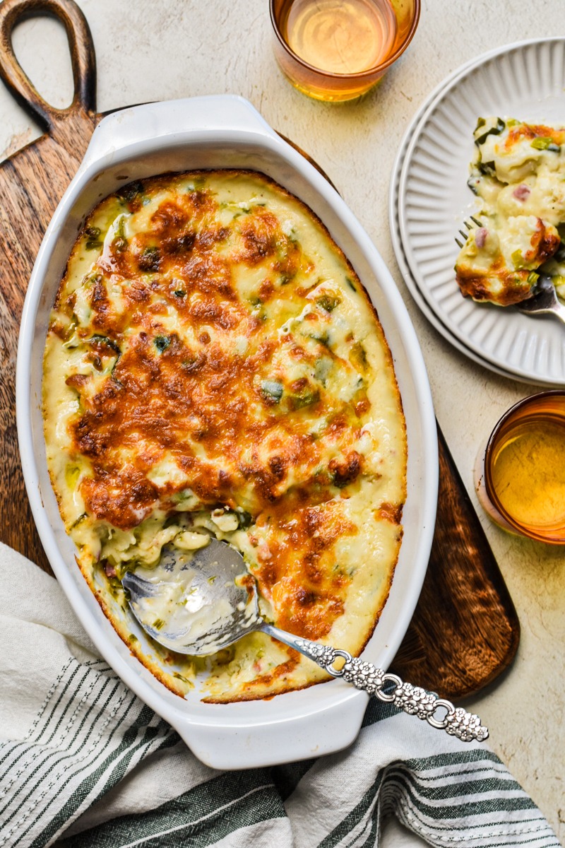 Roasted cauliflower casserole with leeks and pancetta in a baking dish with a serving spoon.