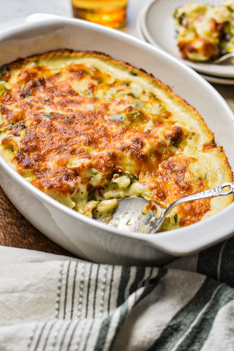 Side view of roasted cauliflower casserole with leeks and pancetta with a serving spoon.