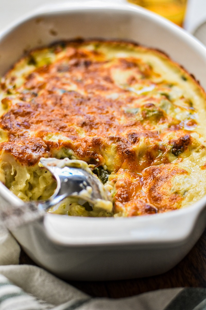 Cheesy roasted cauliflower casserole in a white baking dish with a serving spoon.