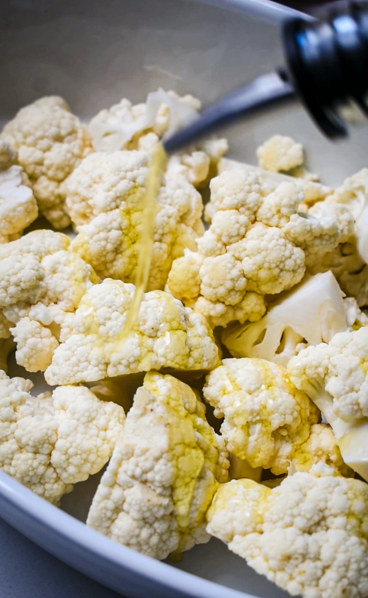 Cauliflower in a bowl being drizzled with olive oil.