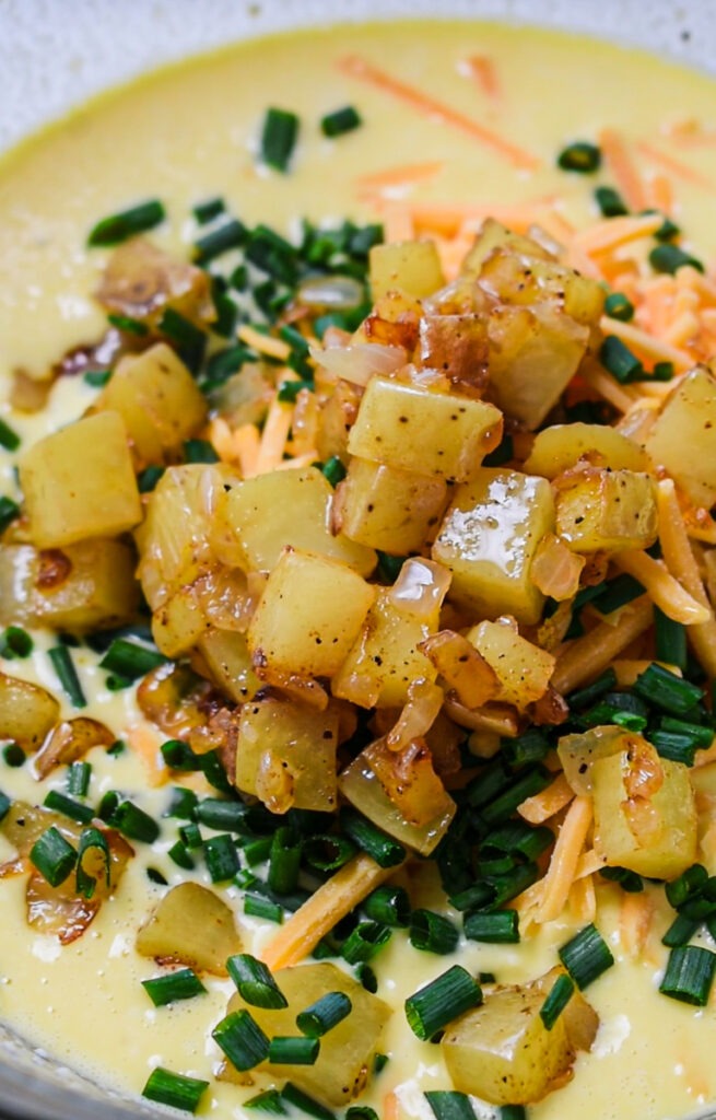 Eggs, cheddar, chives and diced potatoes and onions added to a mixing bowl.