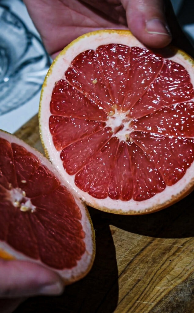 Two halves of a grapefruit cut in half on a wooden board.
