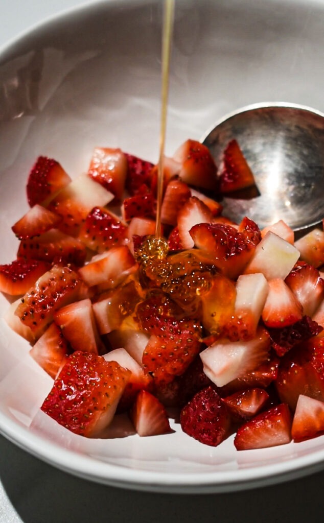 Pouring honey over chopped strawberries in a bowl.