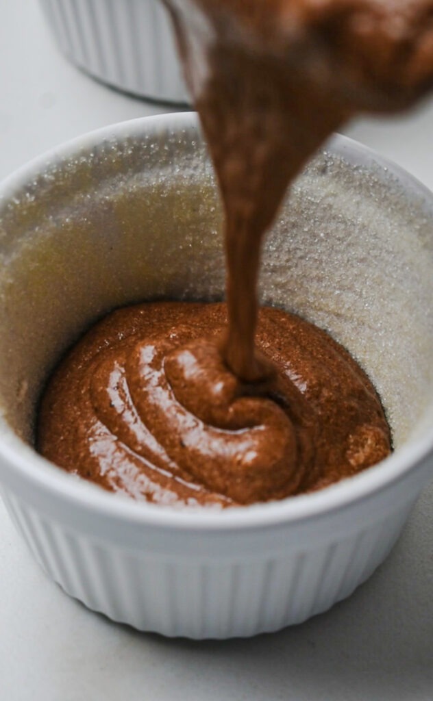 Pouring the chocolate soufflé mixture into a prepared ramekin.