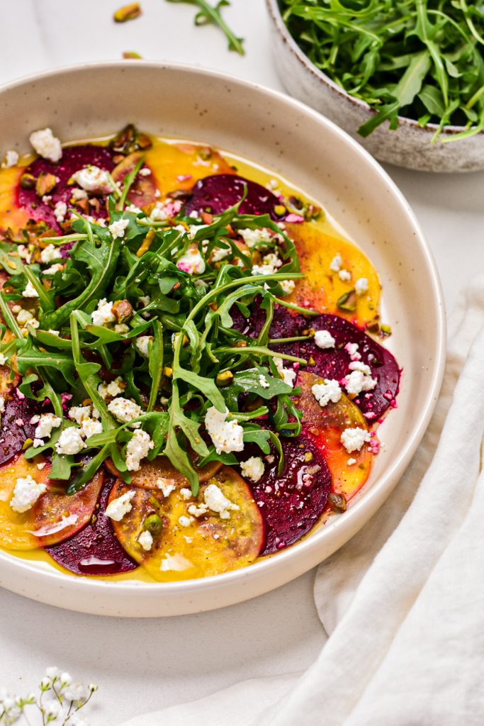 fresh yellow and red raw beet slices arranged on the plate topped with fresh green arugula