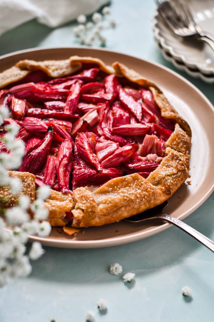 freshly baked rhubarb ginger almond cake topped with fresh rhubarb on a ceramic plate.