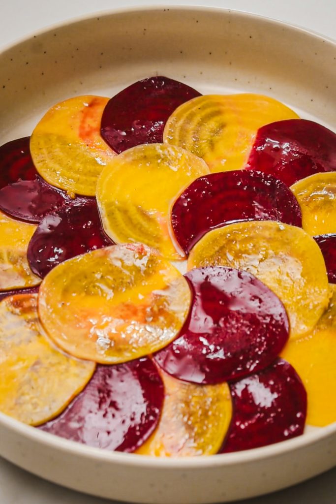 slices of red and yellow raw beet arranged on a plate topped with olive oil