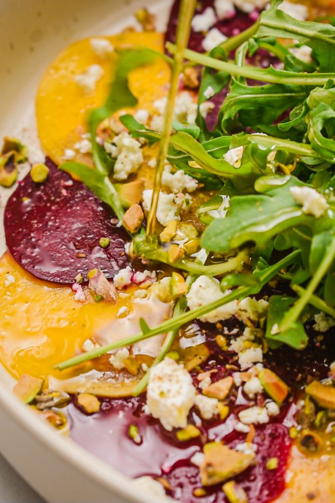 close up of raw beet carpaccio salad topped with fresh arugula leaves
