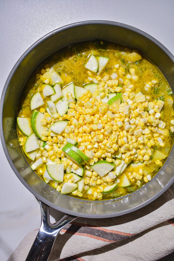 a pot simmering with corn, zucchini and shrimp