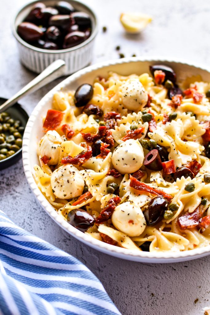 Farfalle Italian pasta salad in a served bowl next to a small bowl of capers.