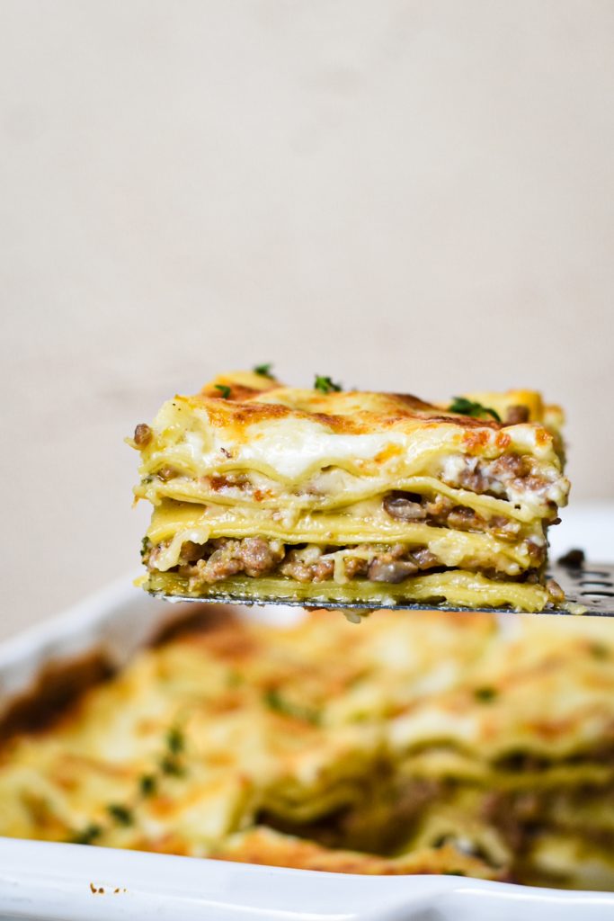 Spatula holding up a slice of lasagna to show the layers with more lasagna in the background.