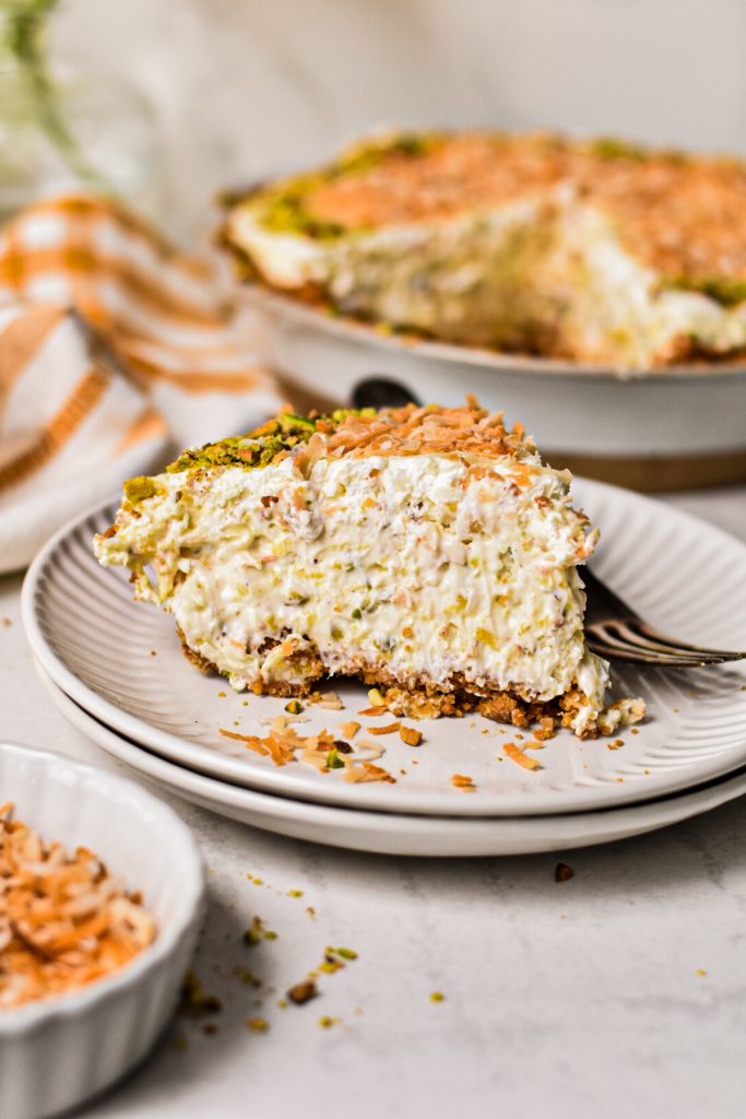 Slice of million dollar pie with pistachio on a plate with the whole pie in the background.