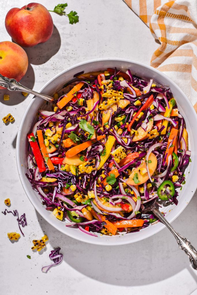 Overhead shot of spicy peach corn summer slaw next to two whole peaches.
