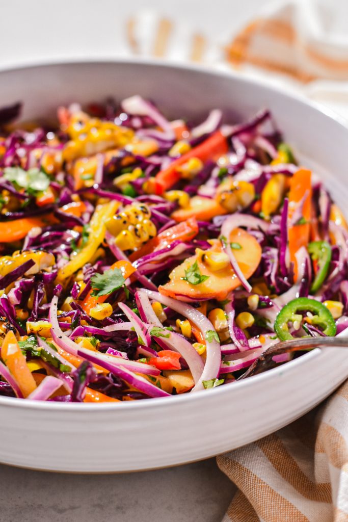 Spicy peach corn summer slaw served in a white serving bowl with a spoon.