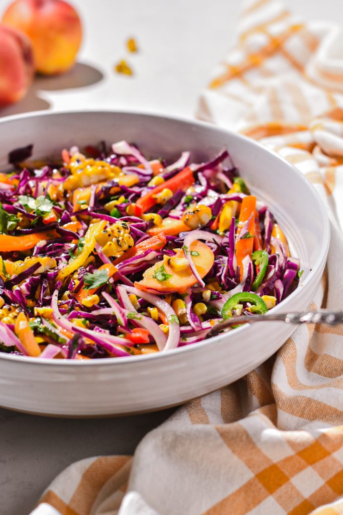 Peach summer slaw served in a large white bowl with a spoon.