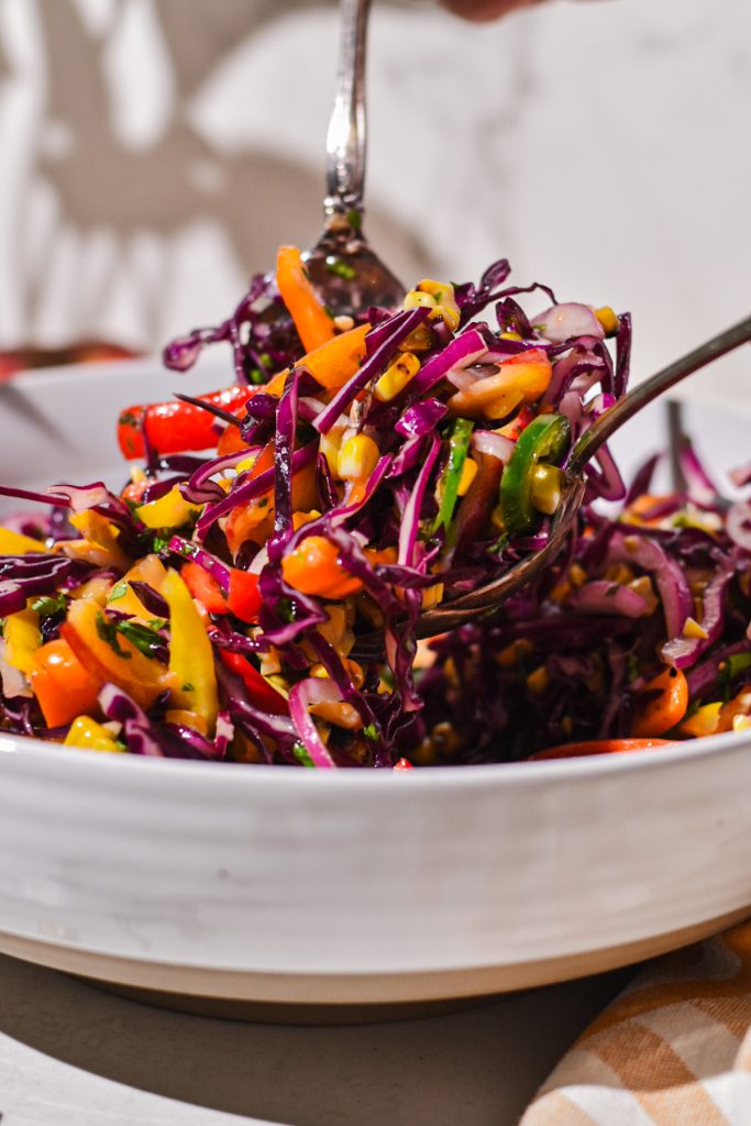 Using two forks to mix together the coleslaw with the dressing.