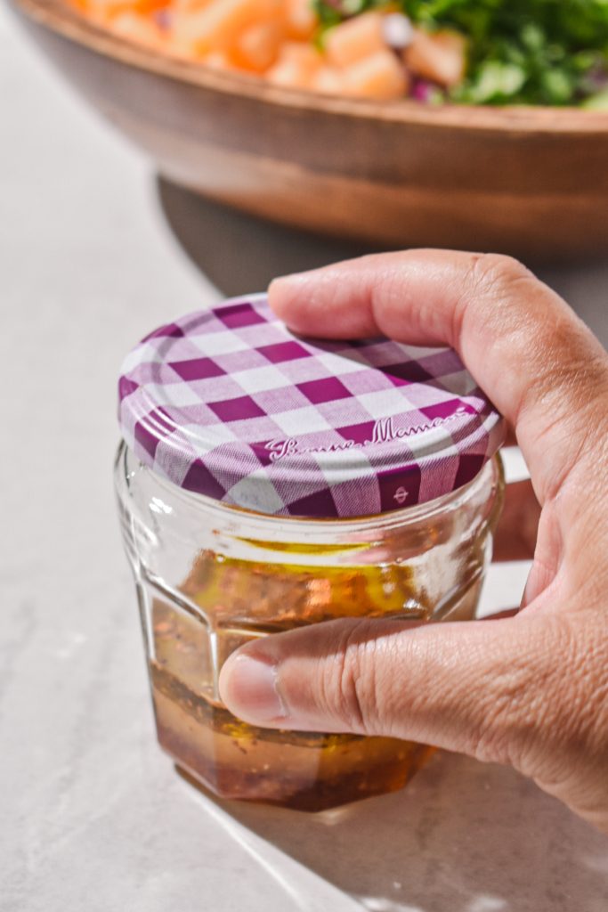 Hand holding a small jar filled with the ingredients for the dressing.